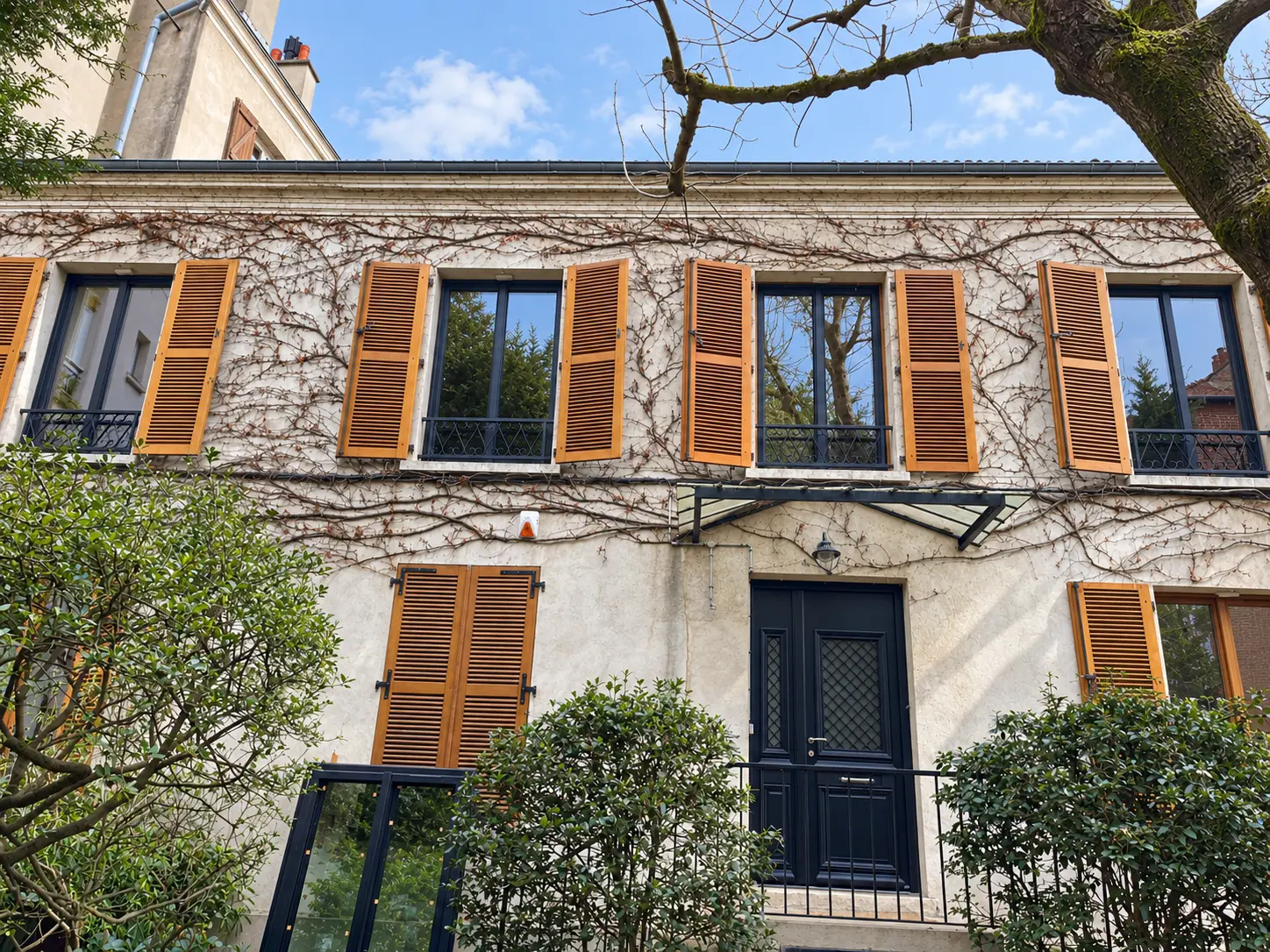 Façade en pierre claire avec fenêtres sombres et volets bois